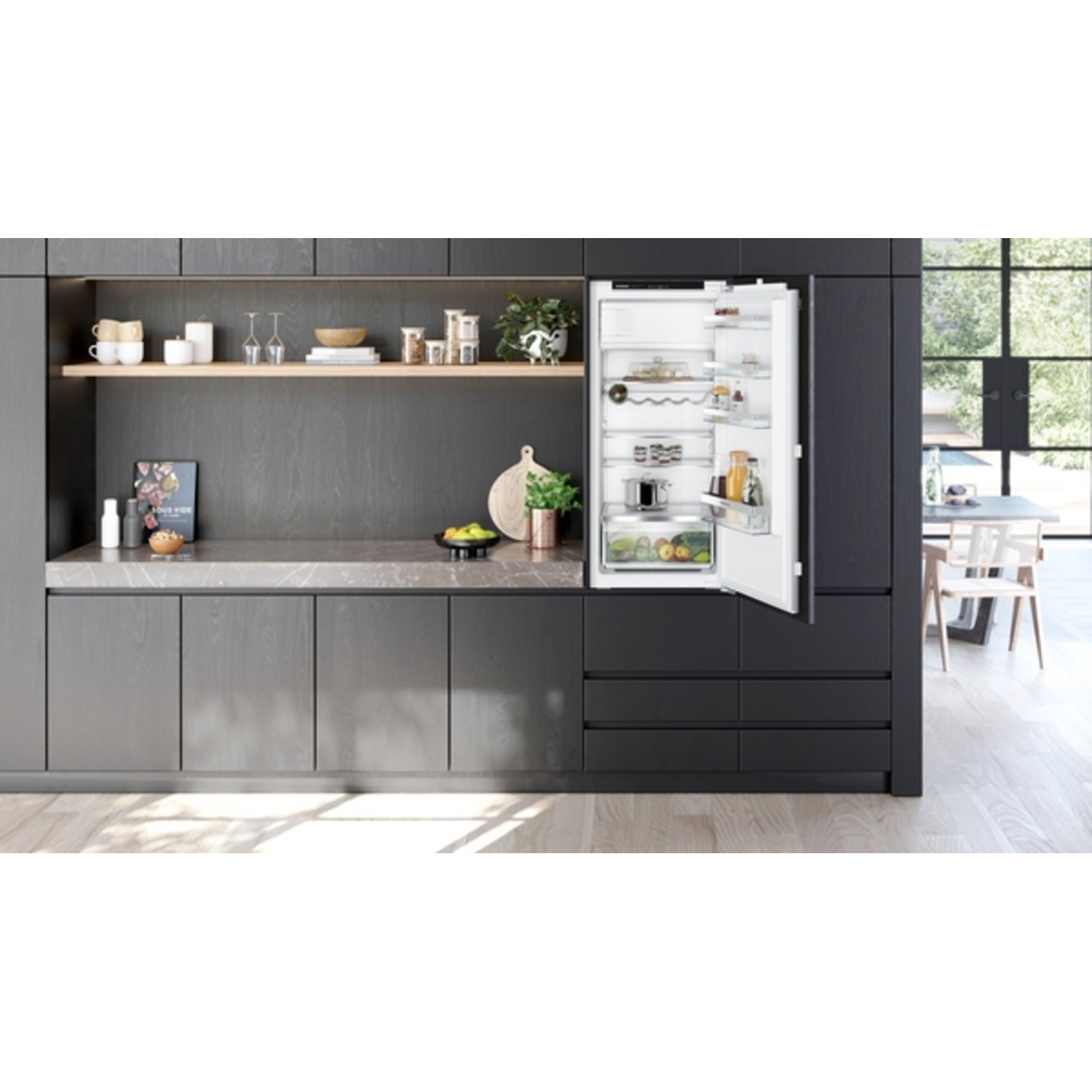 Keukeninterieur met open koelkast, planken met items, donkere kasten en een raam met eethoek.