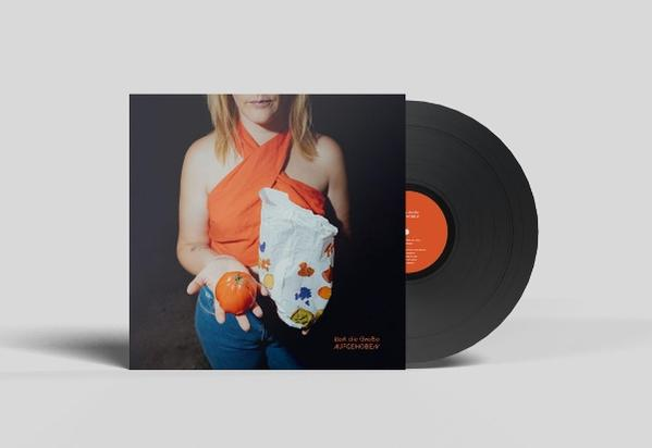 Eine Frau hält eine Tomate und eine Papiertüte. Auf der rechten Seite befindet sich eine Vinyl-Schallplatte. Das Albumcover hat Text und eine Frau.