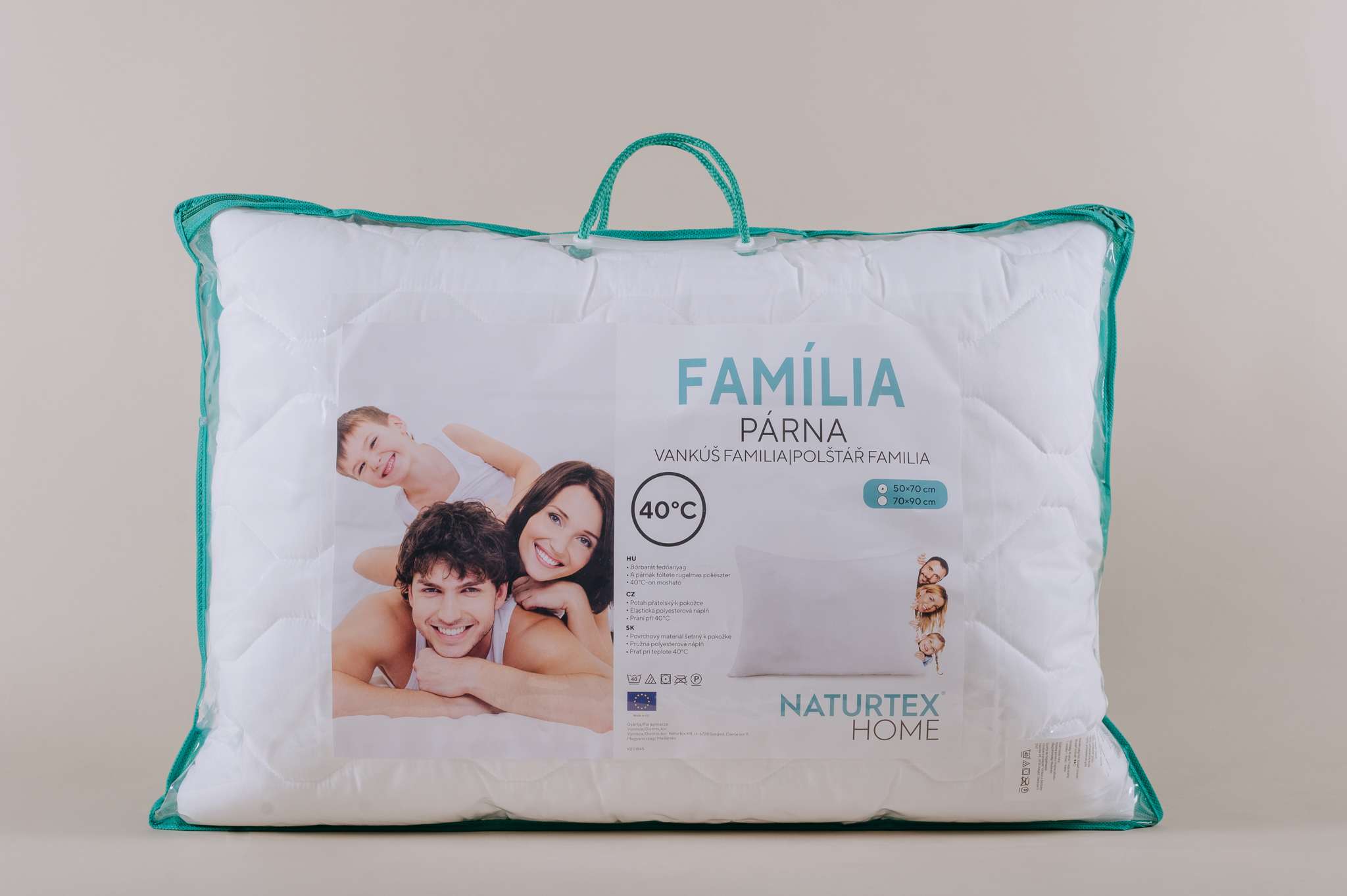 Egy fehér párna átlátszó műanyag zacskóban, családi képpel és szöveggel több nyelven. A szöveg a Familia, Parna és a Naturtex Home.