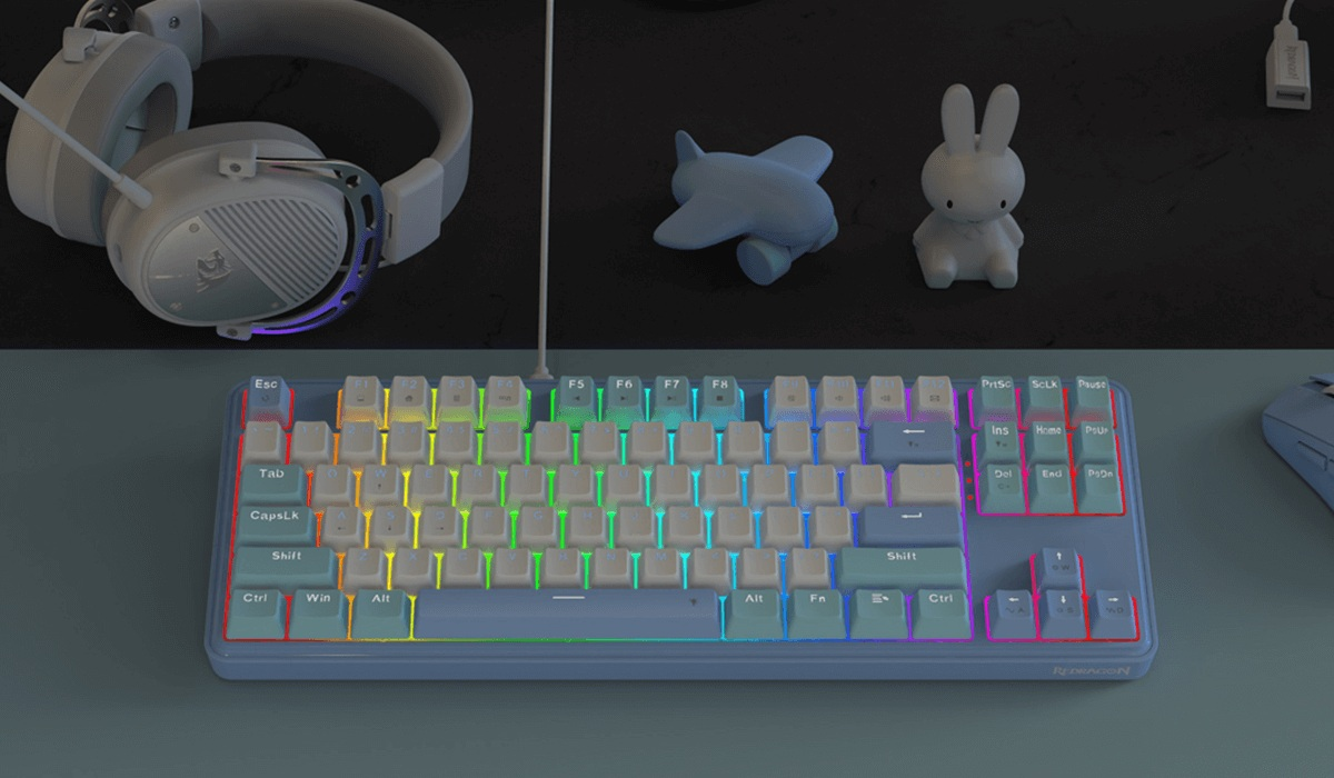 Konfiguracja do gier zawiera klawiaturę z podświetleniem RGB, słuchawki, zabawkę samolotu i figurkę królika na biurku.