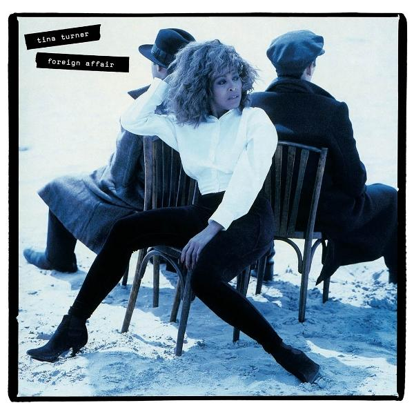 Tina Turner sitzt in einem Stuhl und trägt ein weißes Hemd und eine schwarze Hose. Zwei Männer sind hinter ihr. Albumtitel: 'Foreign Affair'.