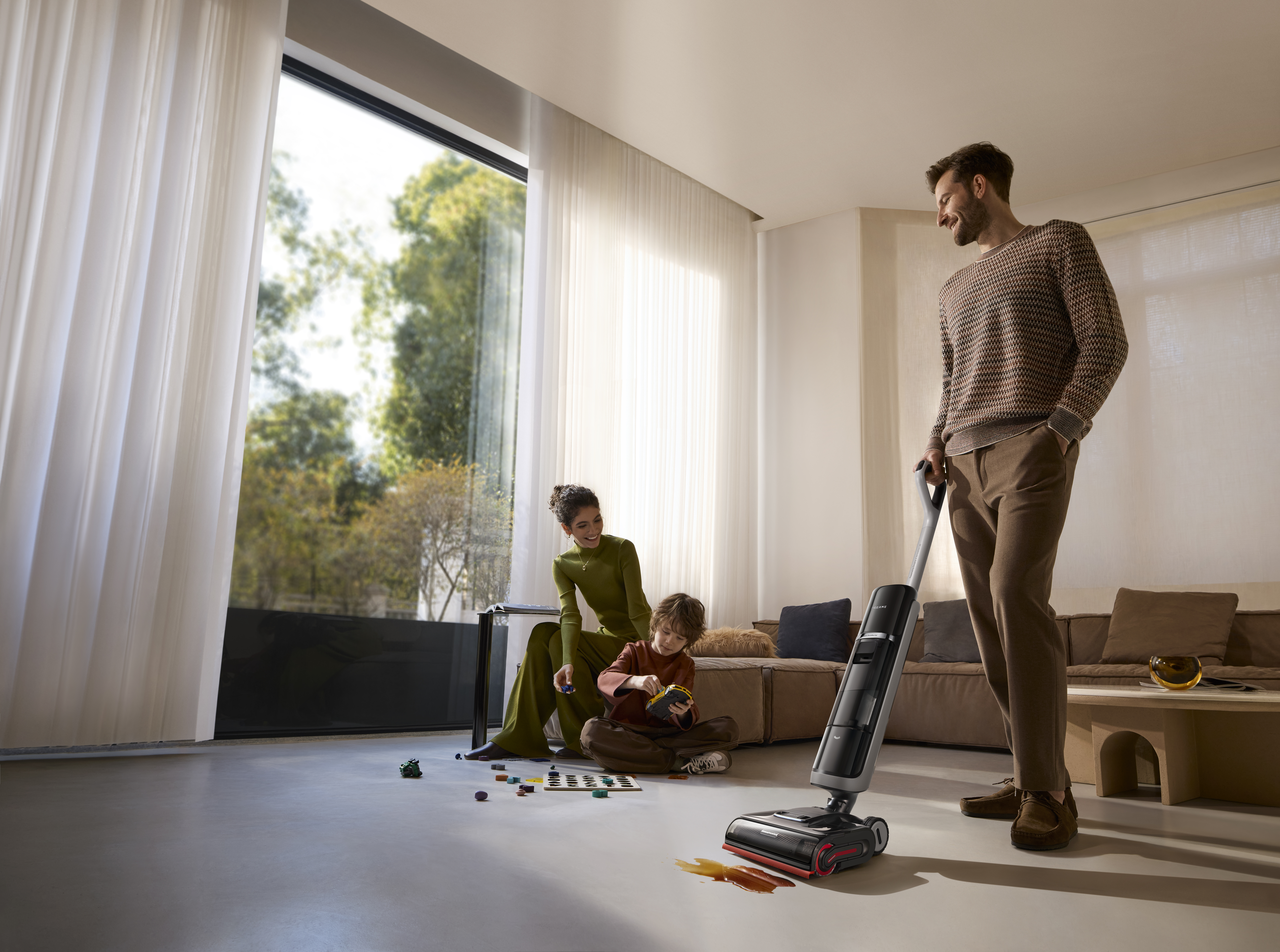 Rodzina w salonie z odkurzaczem. Obecni są mężczyzna, kobieta i dziecko. Mężczyzna używa odkurzacza.