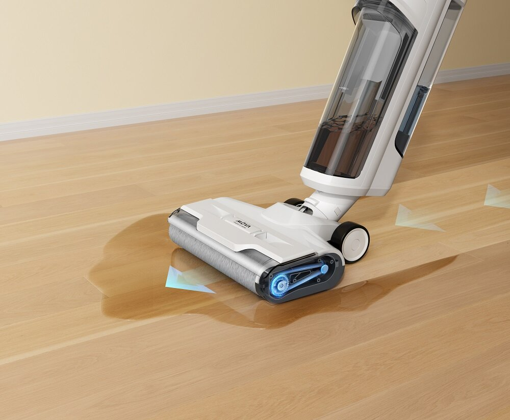 Biało-szara myjka do podłóg na drewnianej podłodze, czyszcząca rozlaną wodę. W tle kremowa ściana.