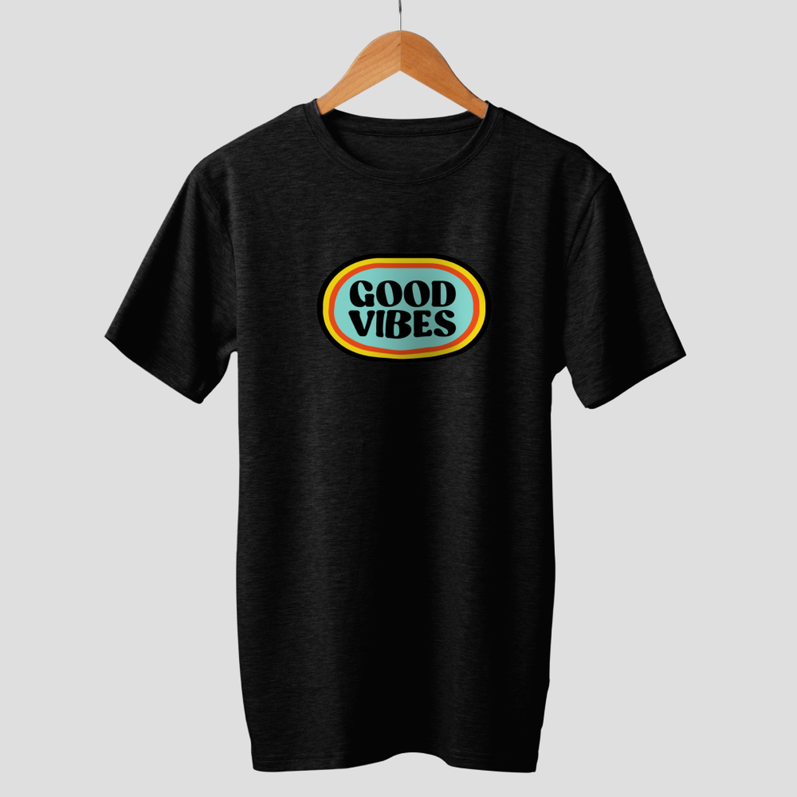 Schwarzes T-Shirt mit ovalem "GOOD VIBES"-Design. Es hängt an einem Holzbügel. Der Hintergrund ist schlicht grau.