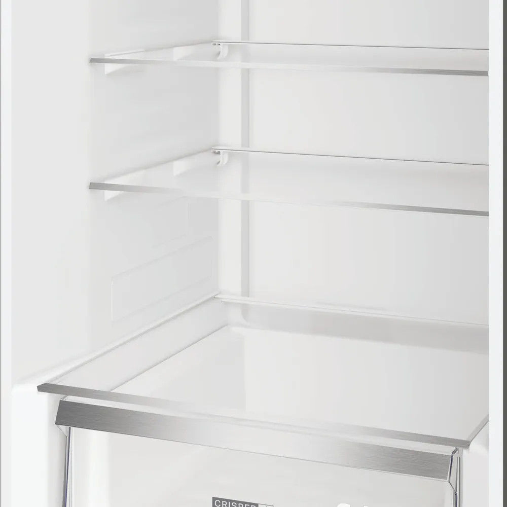 Puste wnętrze lodówki ze szklanymi półkami i dolną szufladą na warzywa. Ściany są białe, a półki są podparte metalowymi ramami.