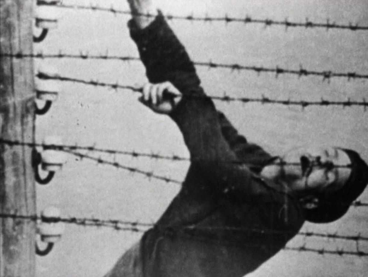Schwarz-Weiß-Bild einer Person, die sich an Stacheldraht festhält. Sie greift mit einem Arm nach oben, möglicherweise in Not.