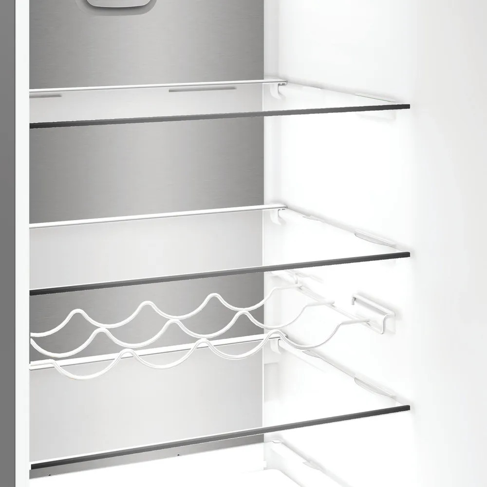 Puste wnętrze lodówki ze szklanymi półkami i stojakiem na wino. Tło to panel ze stali nierdzewnej. Półki są białe.