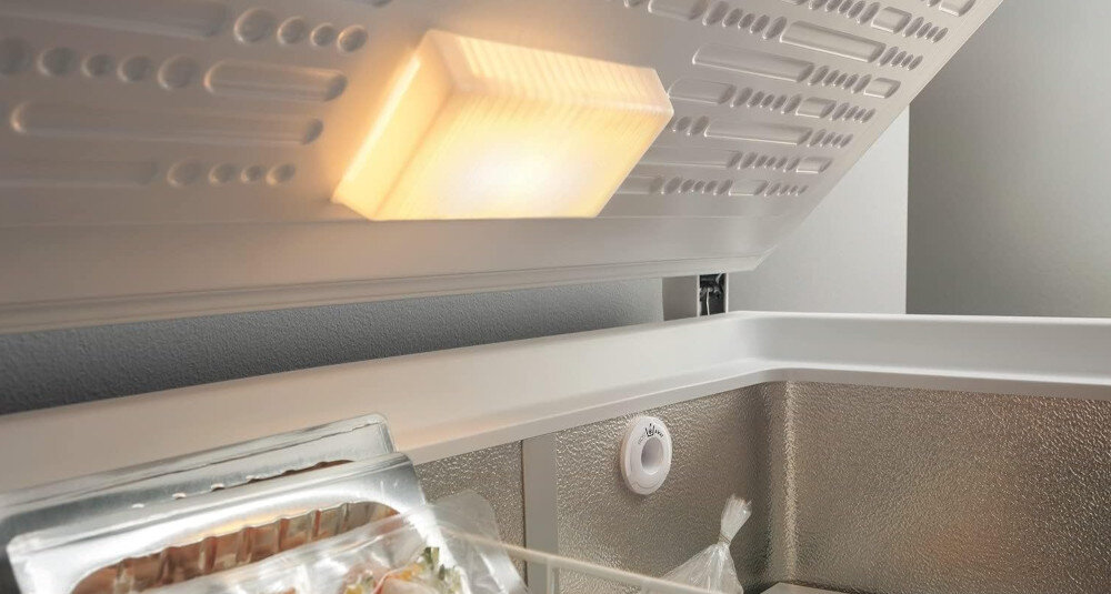 Wewnątrz zamrażarki światło oświetla górę. W pojemnikach znajduje się żywność i biały wskaźnik temperatury.