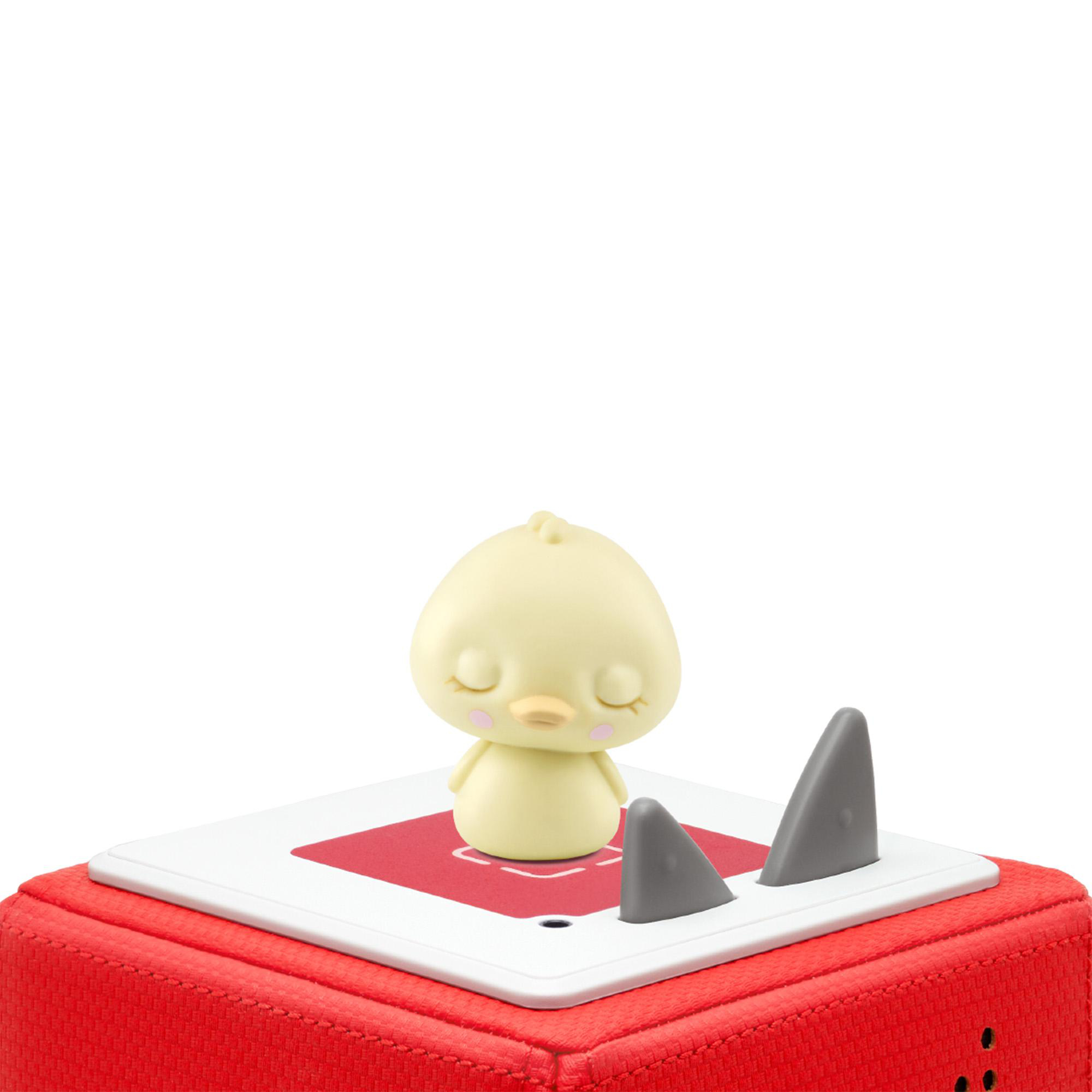 Ein gelbes Küken-Spielzeug mit geschlossenen Augen sitzt auf einer rot-weißen Plattform mit zwei grauen Haifischflossen. Rote Box Basis.