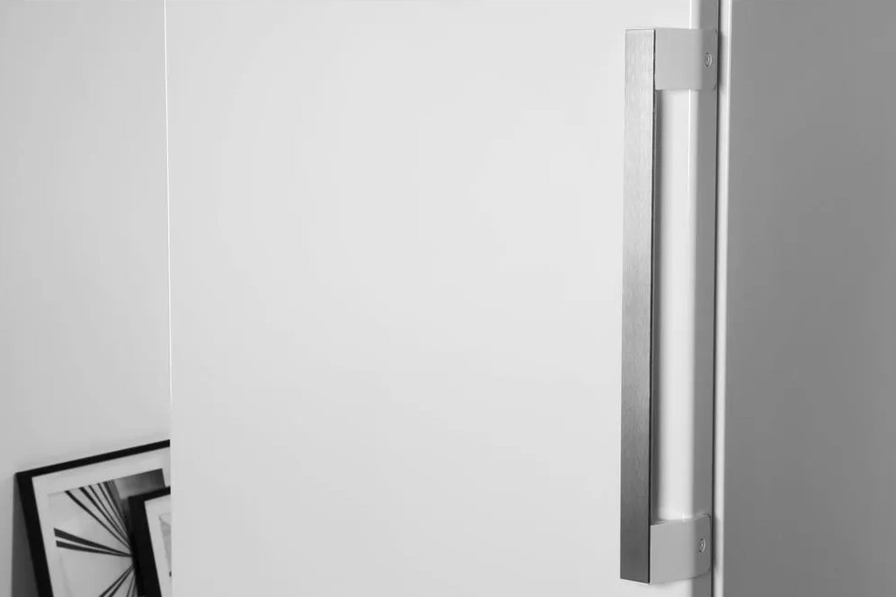 Zbliżenie białych drzwi z pionowym metalowym uchwytem. Ramka na zdjęcia widoczna w lewym dolnym rogu.