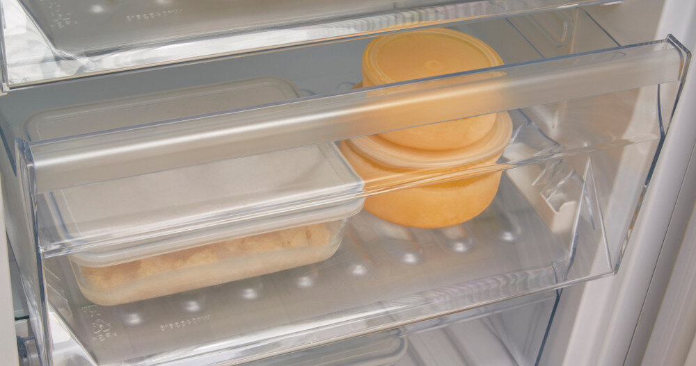 Wnętrze lodówki z przezroczystymi pojemnikami. Jeden ma pokrywkę i żółtą zawartość, drugi białą pokrywkę i beżową zawartość.