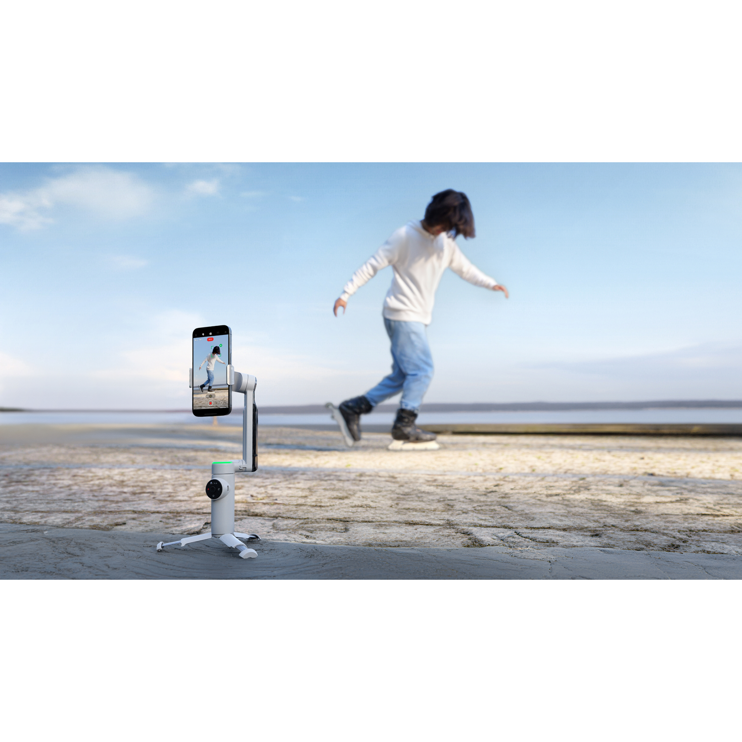 Een persoon die schaatst, bewegingsonscherpte. Een telefoon neemt de scène op. Heldere blauwe lucht, wit statief en een bevroren meer op de achtergrond.