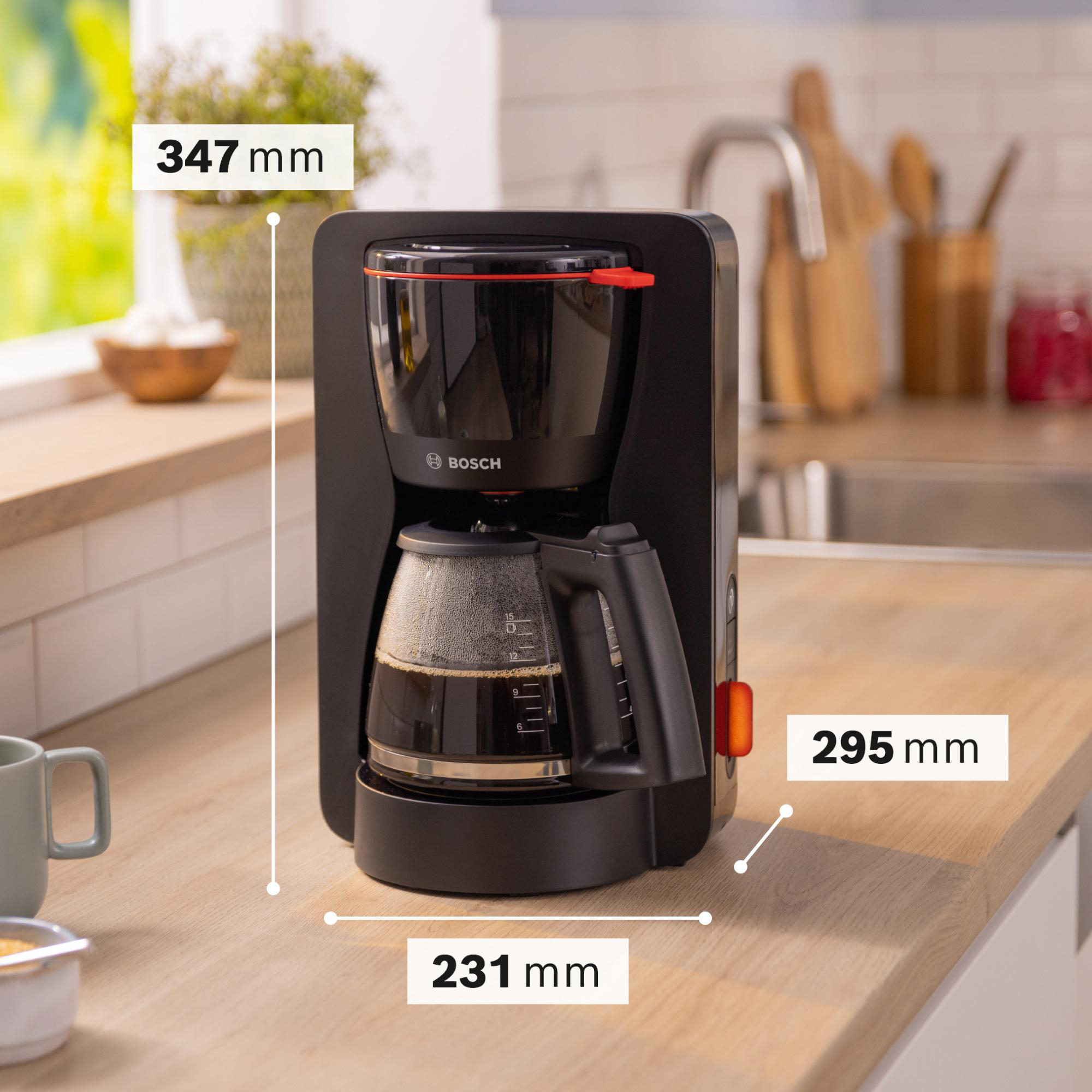 Eine schwarze Bosch Kaffeemaschine auf einer Holztheke, mit Maßangaben. Eine Tasse und eine Schüssel sind im Vordergrund.