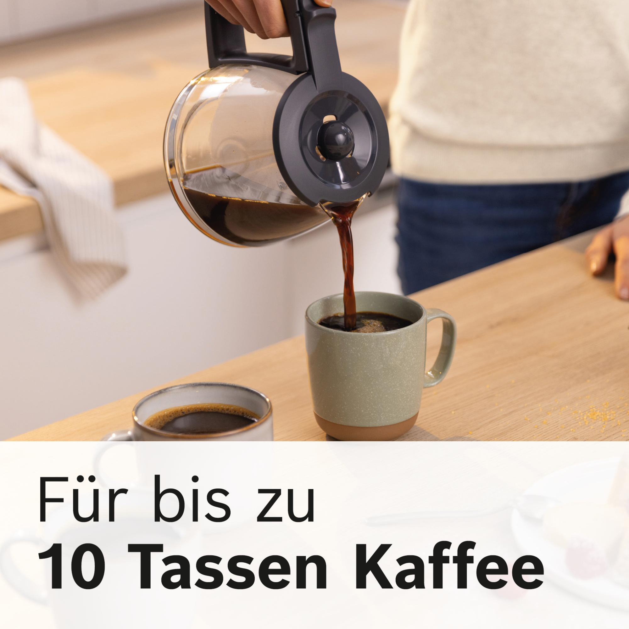 Kaffee wird in eine grüne Tasse gegossen. Eine zweite, mit Kaffee gefüllte Tasse steht daneben. Szene auf Holzoberfläche.