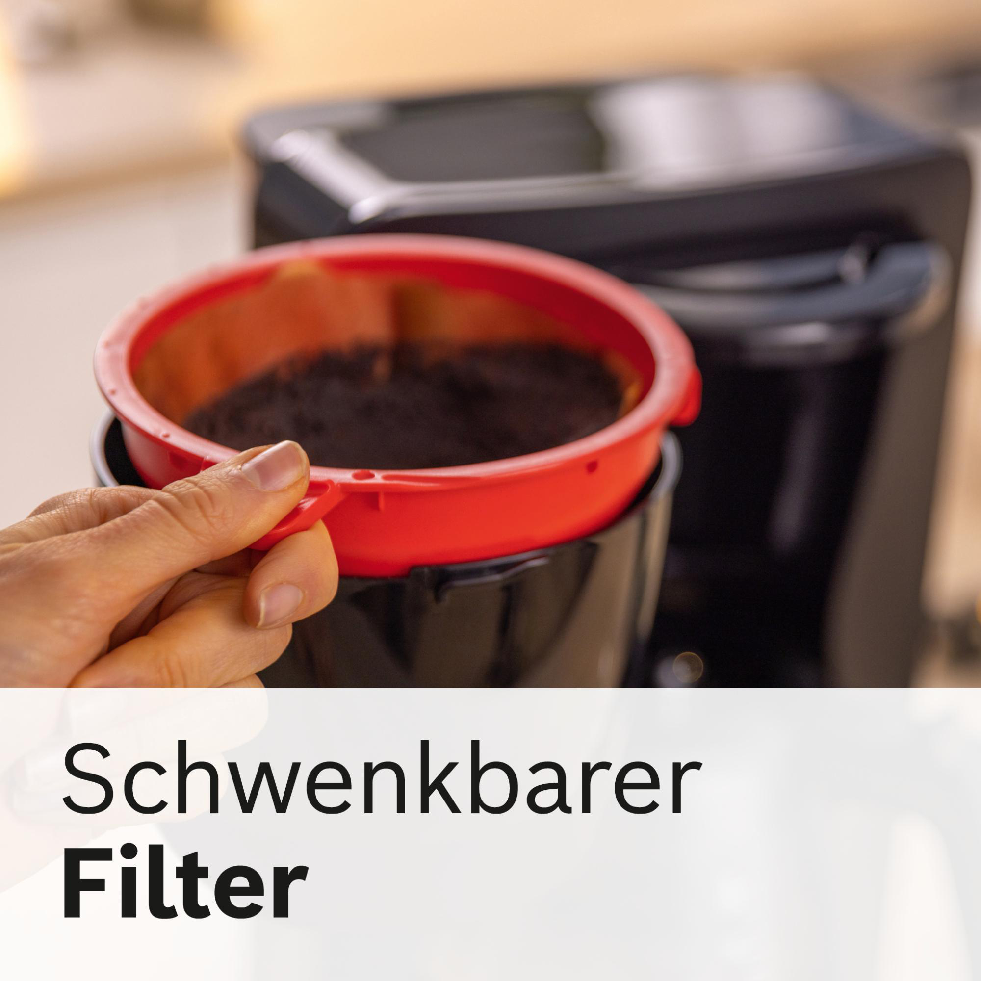 Eine Hand hält einen roten Kaffeefilter mit Kaffeesatz, der in einer schwarzen Kaffeemaschine platziert ist. Der Filter ist bereit zum Schwenken.
