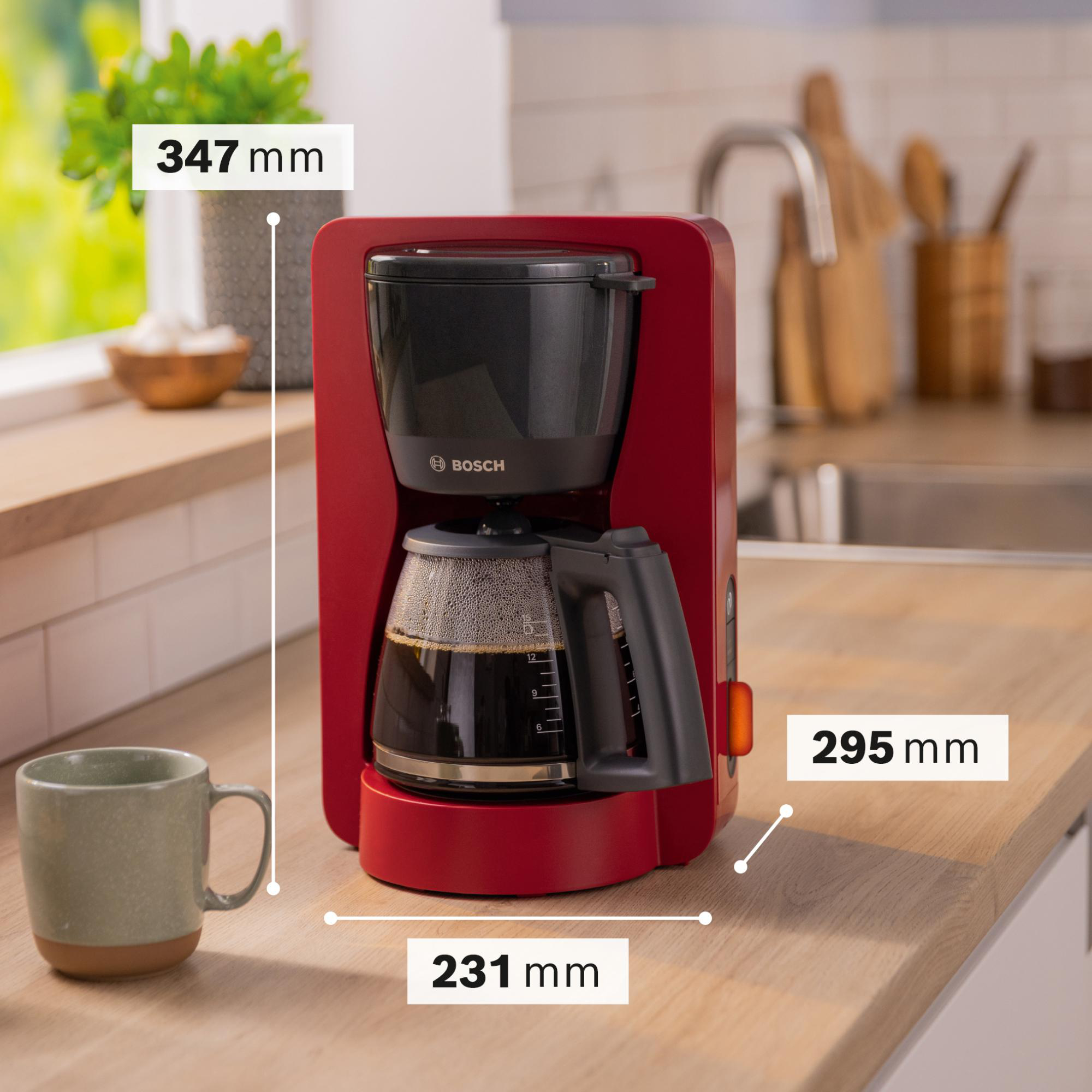 Roter Bosch-Kaffeeautomaten auf einer Arbeitsplatte. Links steht eine Tasse. Maße werden angezeigt.