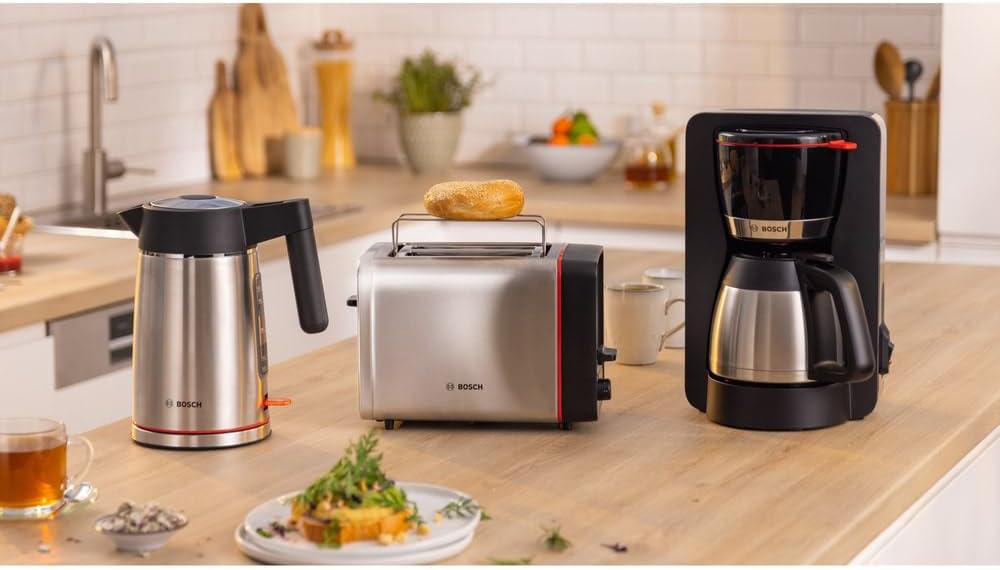 Küchenszene mit Bosch-Geräten: Wasserkocher, Toaster mit Bagel und Kaffeemaschine. Ein Teller mit Essen und Tee im Vordergrund.