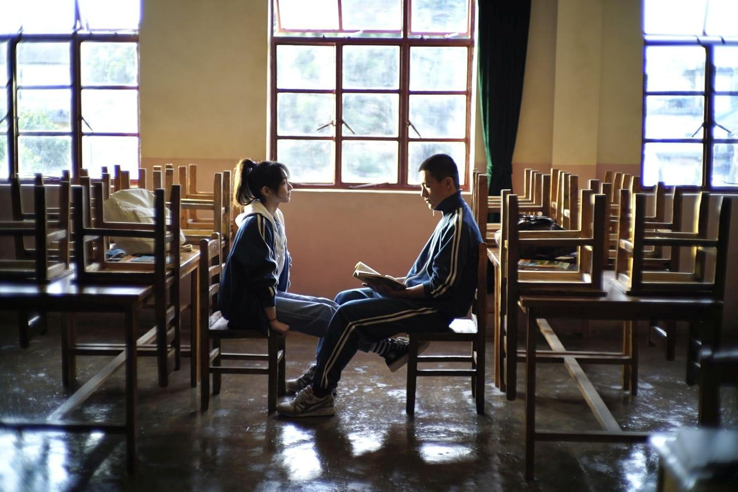 Zwei Studenten sitzen in einem Klassenzimmer. Einer liest ein Buch. Fenster und Stühle sind im Hintergrund. Der Boden ist nass.