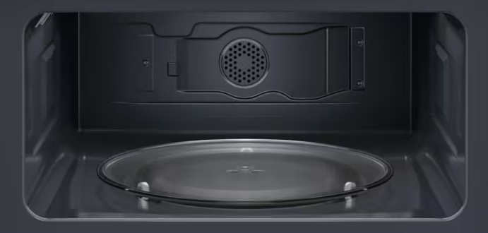 Wnętrze kuchenki mikrofalowej. Szklany talerz na dole. Ciemne wnętrze z wentylacją i innymi elementami u góry.