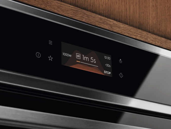 Zbliżenie panelu sterowania piekarnika z cyfrowym wyświetlaczem. Wyświetlacz pokazuje czas gotowania i ustawienia mocy. Drewniana powierzchnia w tle.