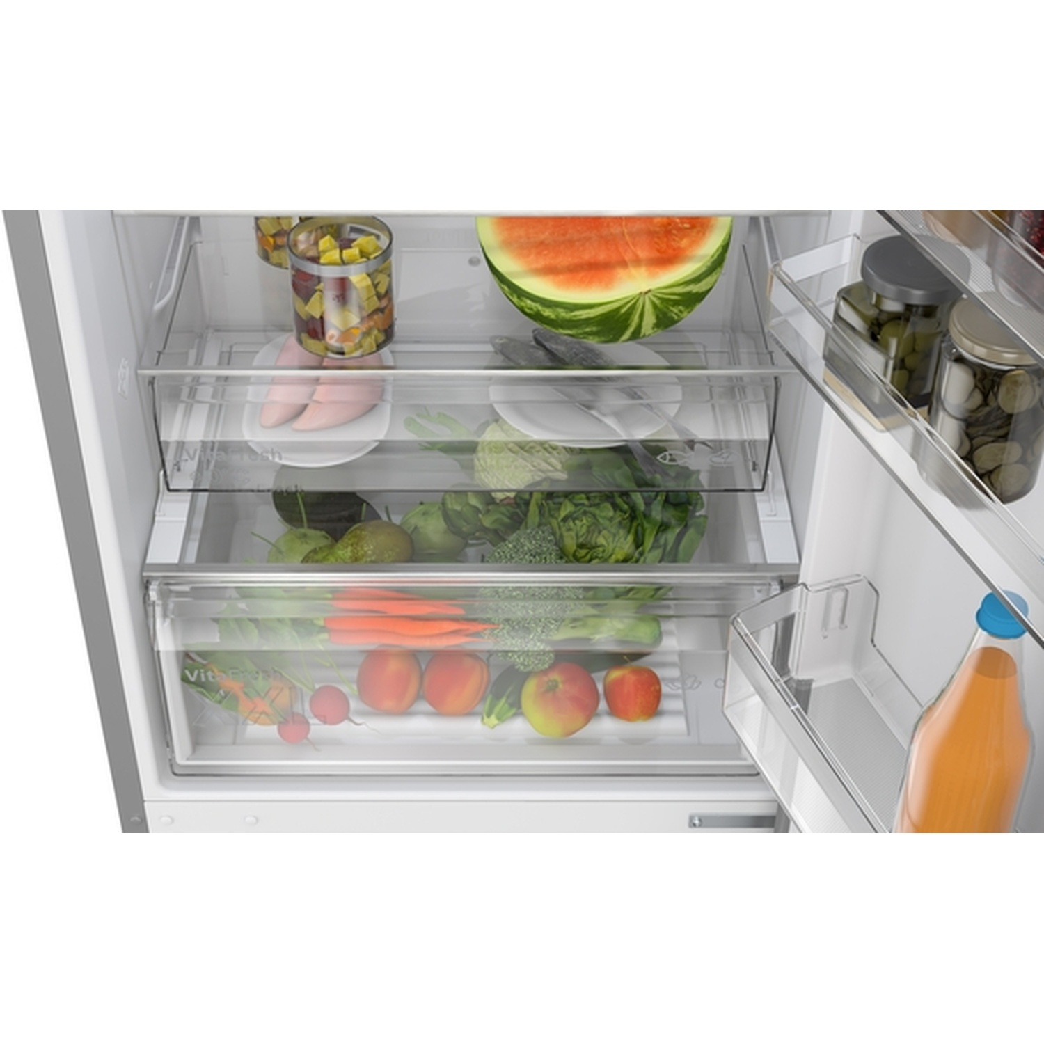 Refrigerator interior with watermelon, vegetables, fruits, jars of pickles, and a bottle of juice. Clear drawers.