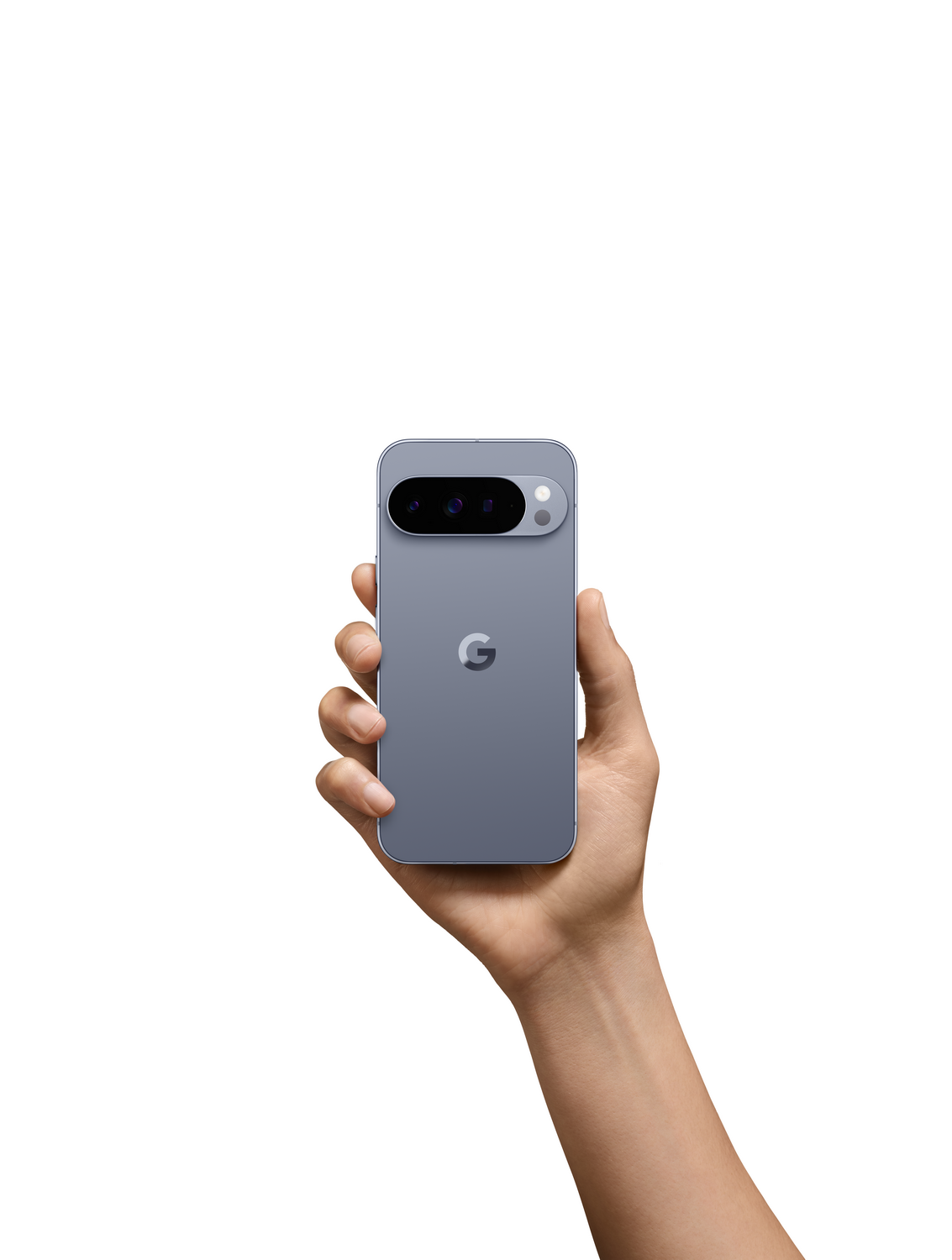 Una mano sostiene un smartphone gris, mostrando la parte trasera. El teléfono tiene una matriz de cámara y un logotipo de Google. Fondo blanco.