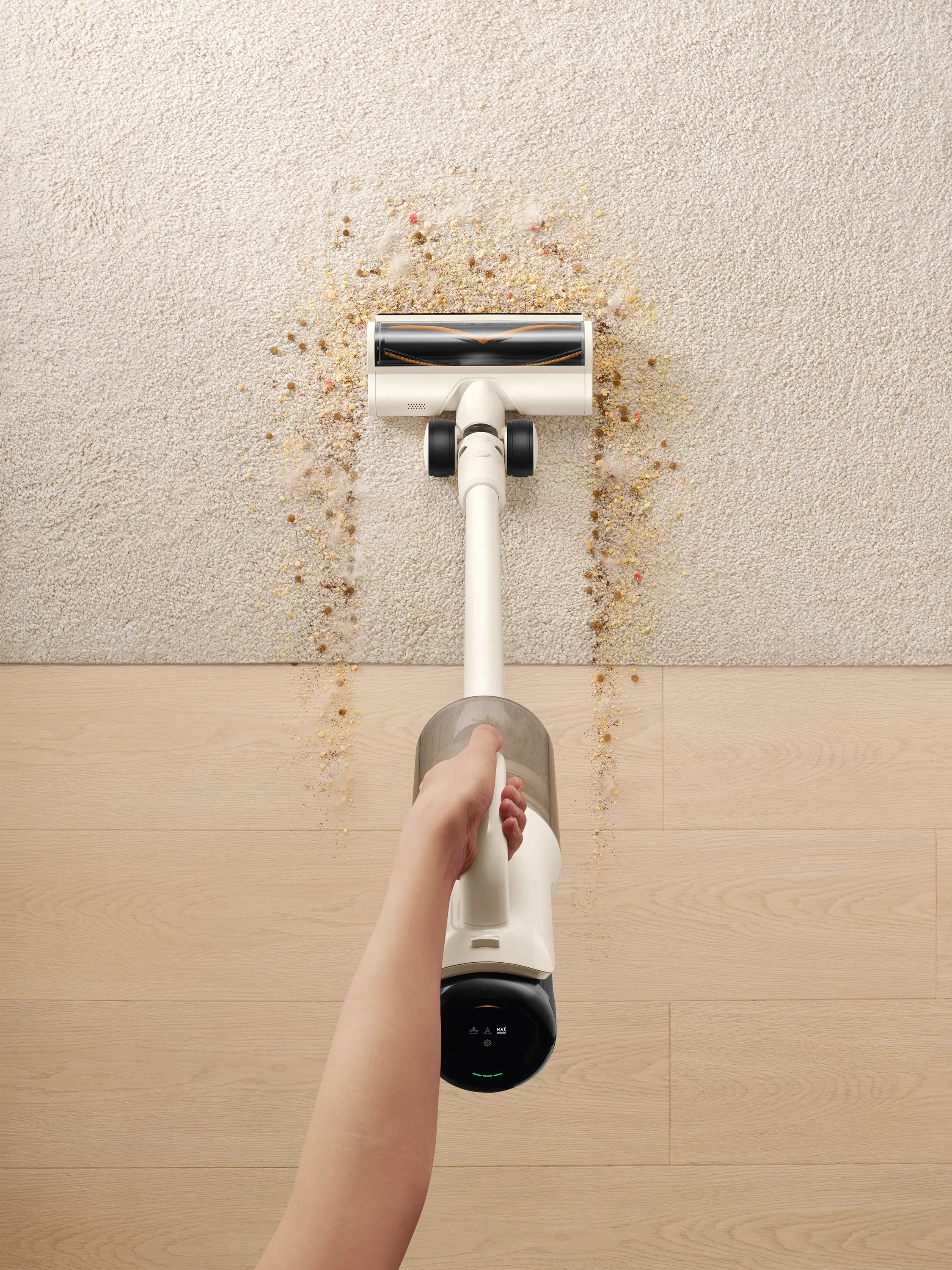 Ręka trzyma odkurzacz nad brudnym dywanem. Na dywanie leżą resztki, a w tle drewniana podłoga.