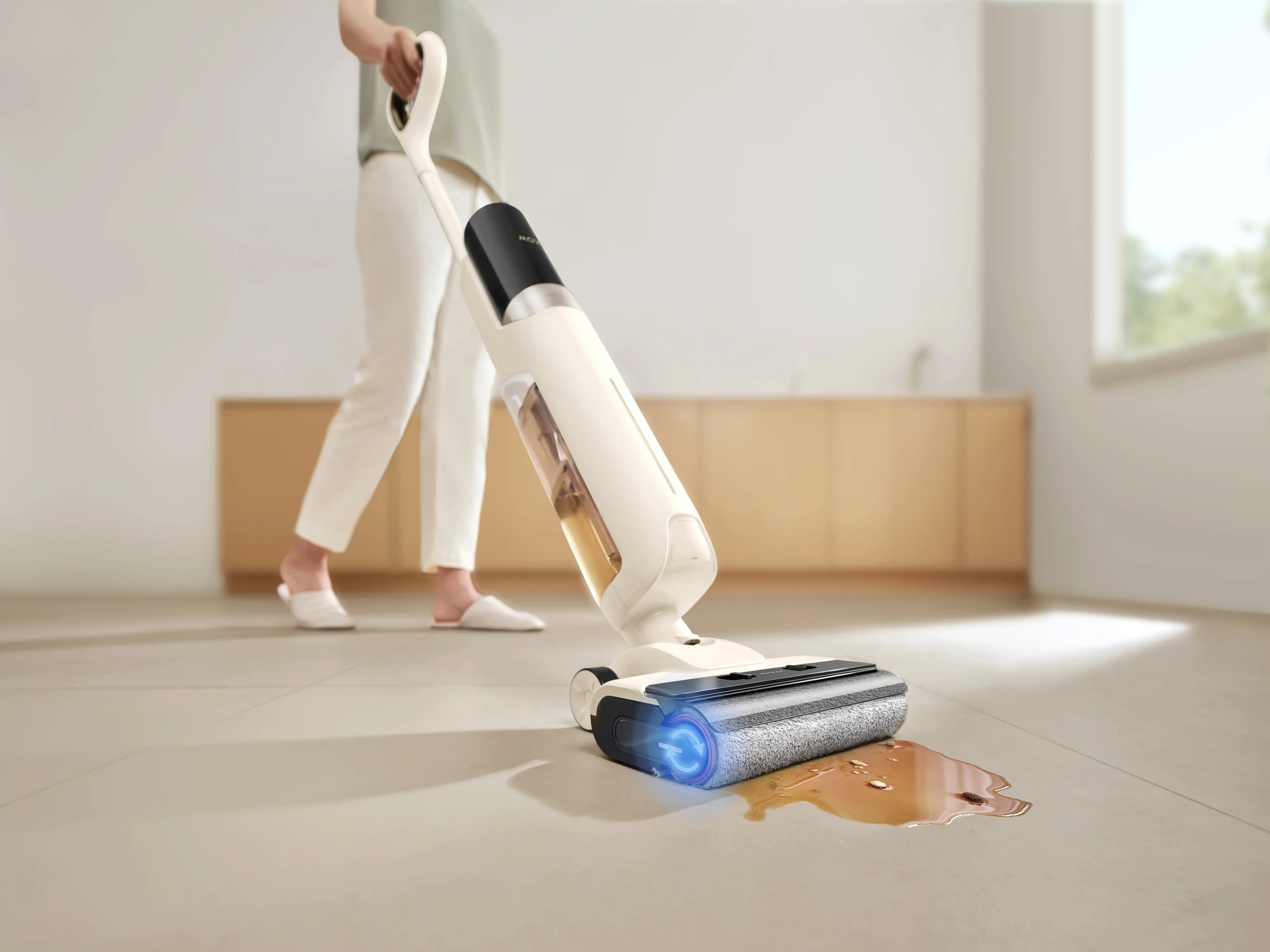 Osoba używa biało-czarnej myjki do podłóg na kafelkach, czyszcząc rozlaną brązową ciecz. Tło obejmuje szafkę.