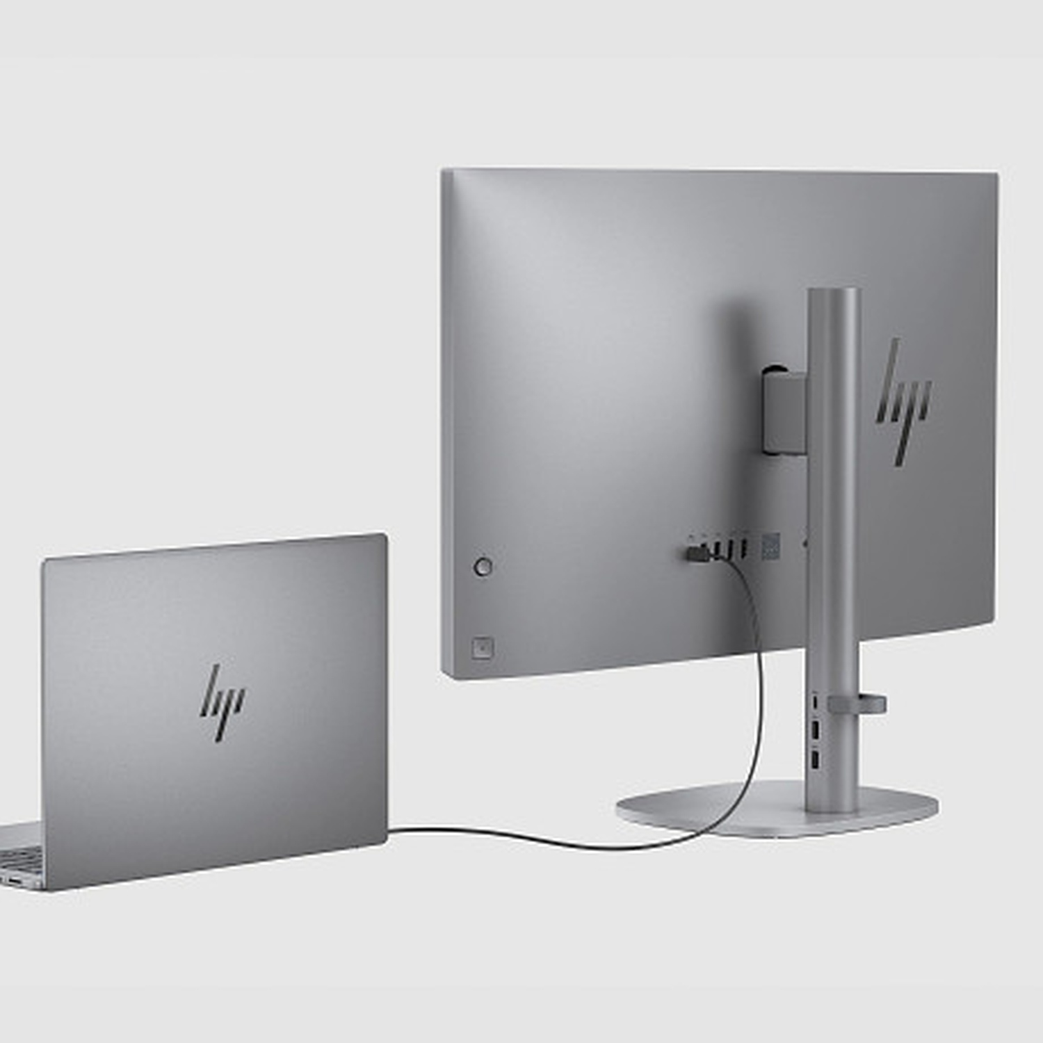 Un ordinateur portable HP argenté est connecté à un moniteur argenté. Le moniteur porte le logo HP et est sur un support. Le fond est blanc.