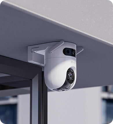 Biała kamera bezpieczeństwa jest zamontowana na białym wsporniku pod szarym okapem. Kamera ma dwa obiektywy i czarny przód.