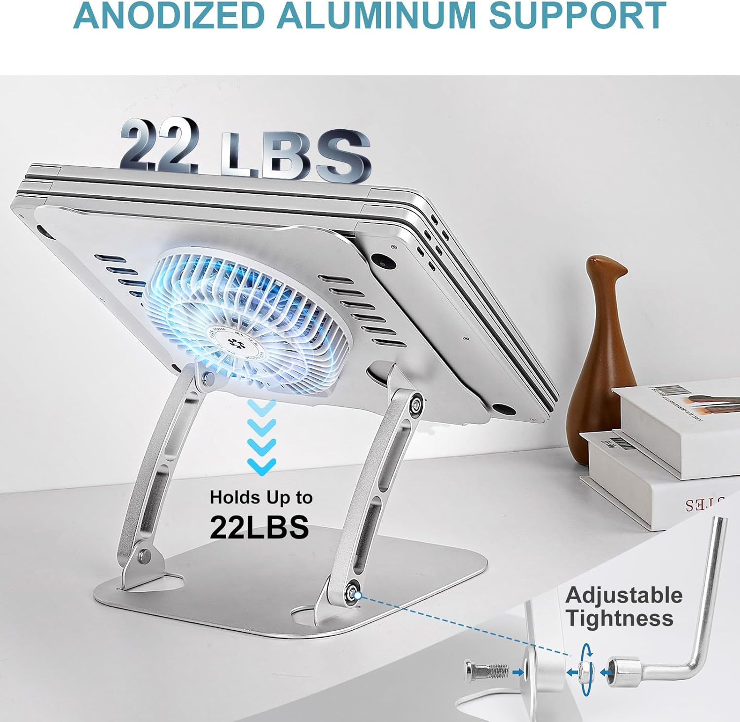 Gümüş laptop standı, fanlı. 22 lbs'ye kadar taşır. Ayarlanabilir sıkılık. Ahşap dekoratif öğe ve kitaplar arka planda.