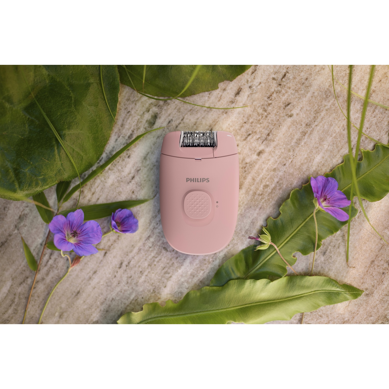 Pink Philips epilator on a textured surface with green leaves and purple flowers.