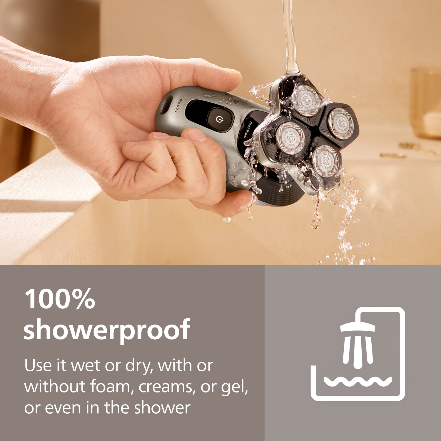 A hand holds a silver electric shaver under running water. The shaver is black and silver, with water splashing around it.