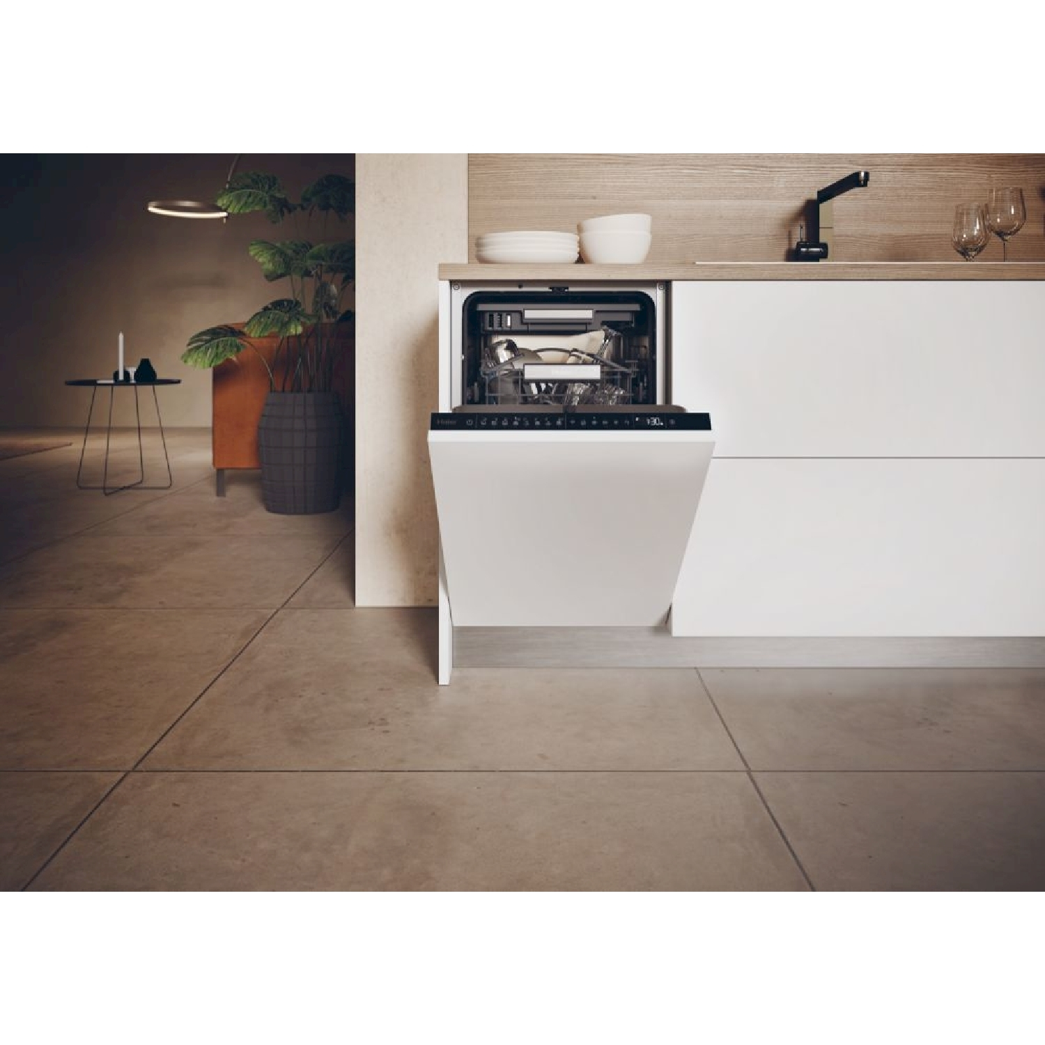 Una lavastoviglie aperta in una cucina moderna. Piatti all'interno. Piante sullo sfondo. Pavimento marrone.