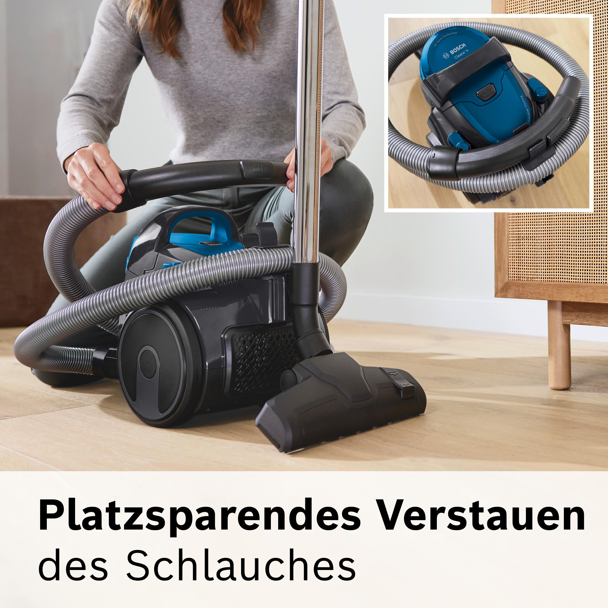 Eine Person hält den Staubsaugerschlauch. Ein blau-schwarzer Staubsauger steht auf dem Holzboden. Ein kleines Bild des Staubsaugers.
