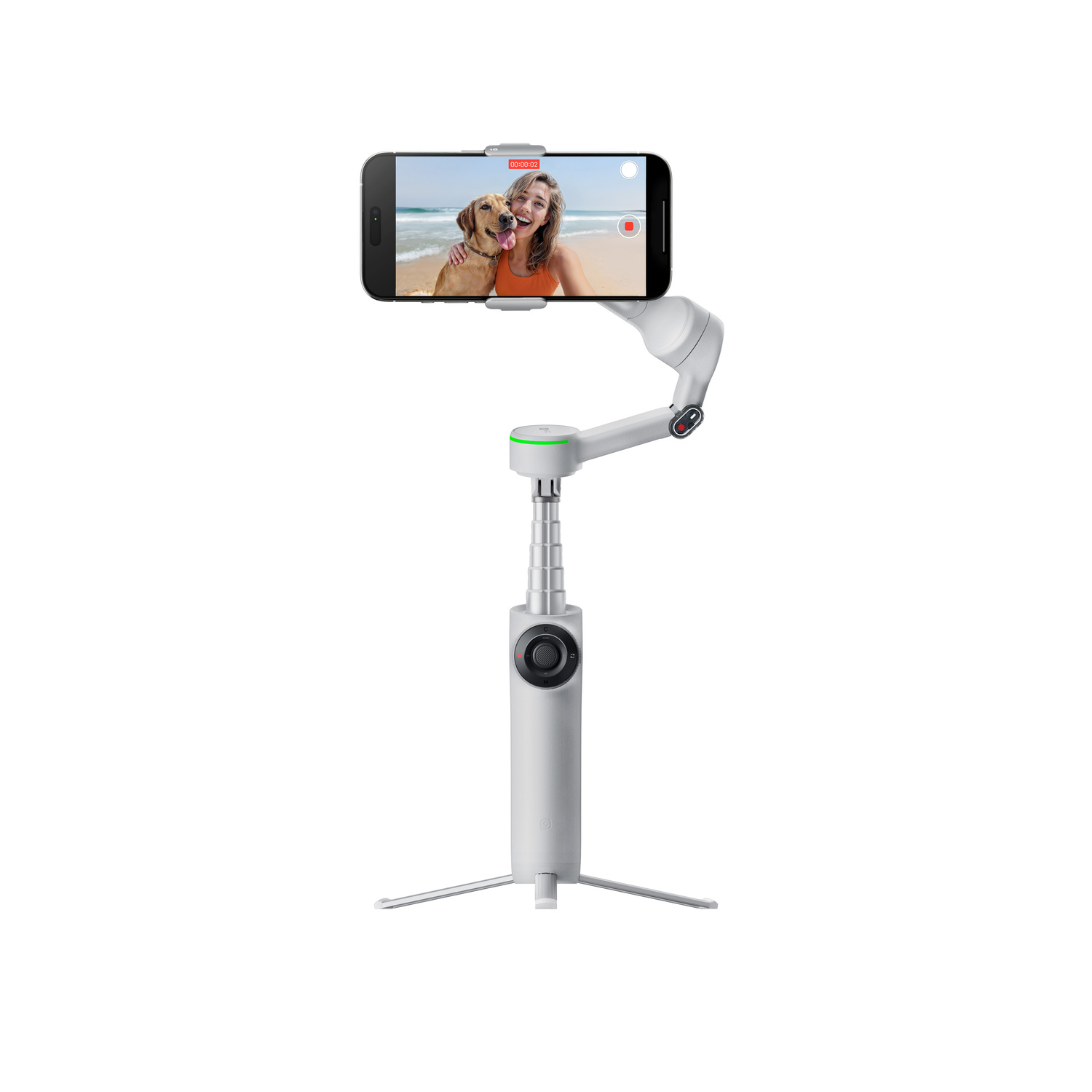 A phone on a white gimbal records a woman and a dog at the beach. The gimbal has a tripod base and an extendable arm.