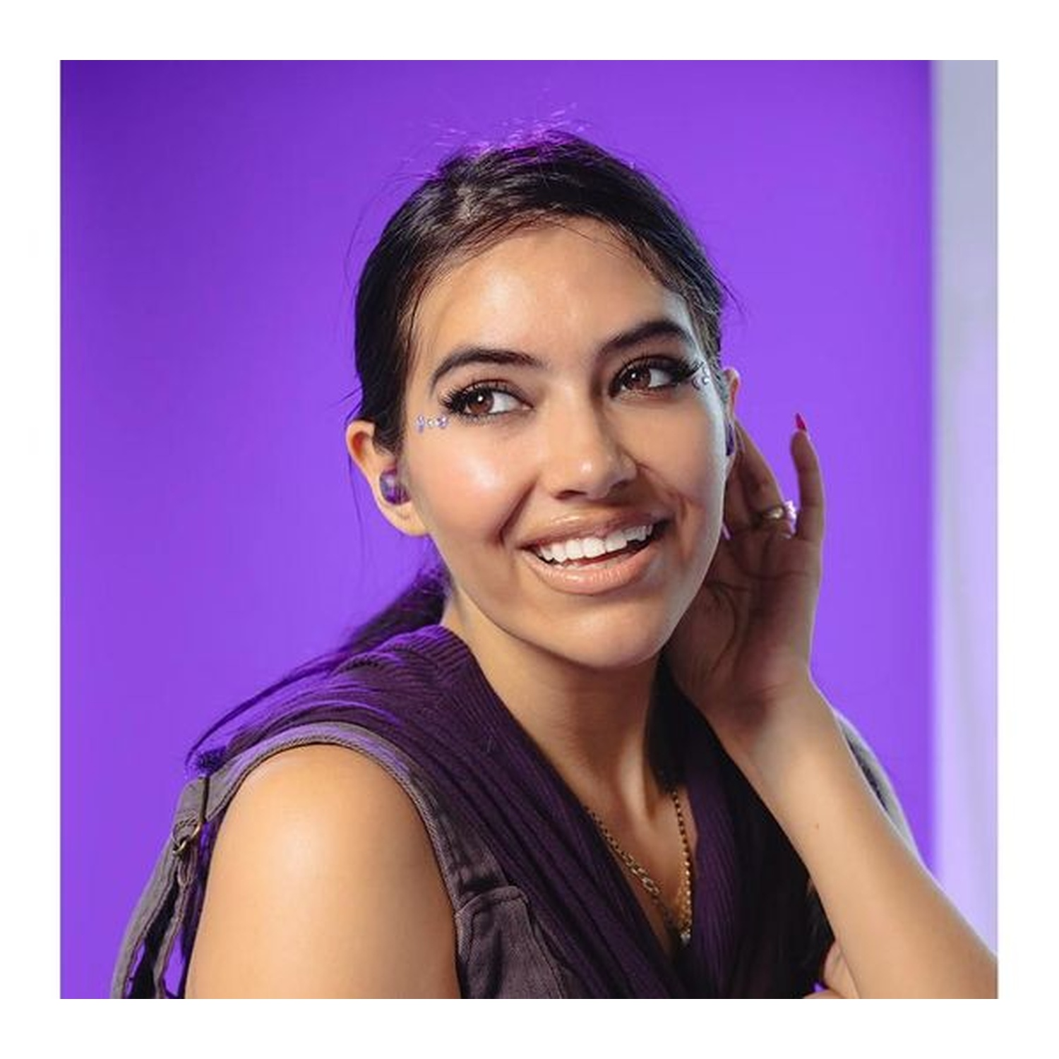 A smiling woman with brown hair and eyes, wearing a purple top, and earrings, with a purple background.