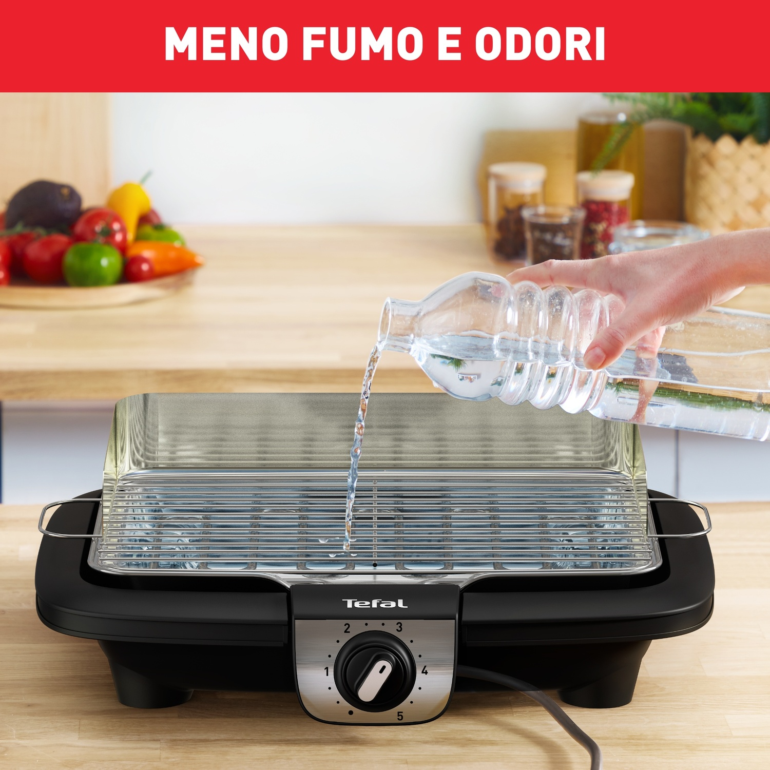 Una persona versa acqua in una griglia Tefal. Verdure a sinistra. La griglia è su una superficie in legno. Il testo "MENO FUMO E ODORI" è in alto.