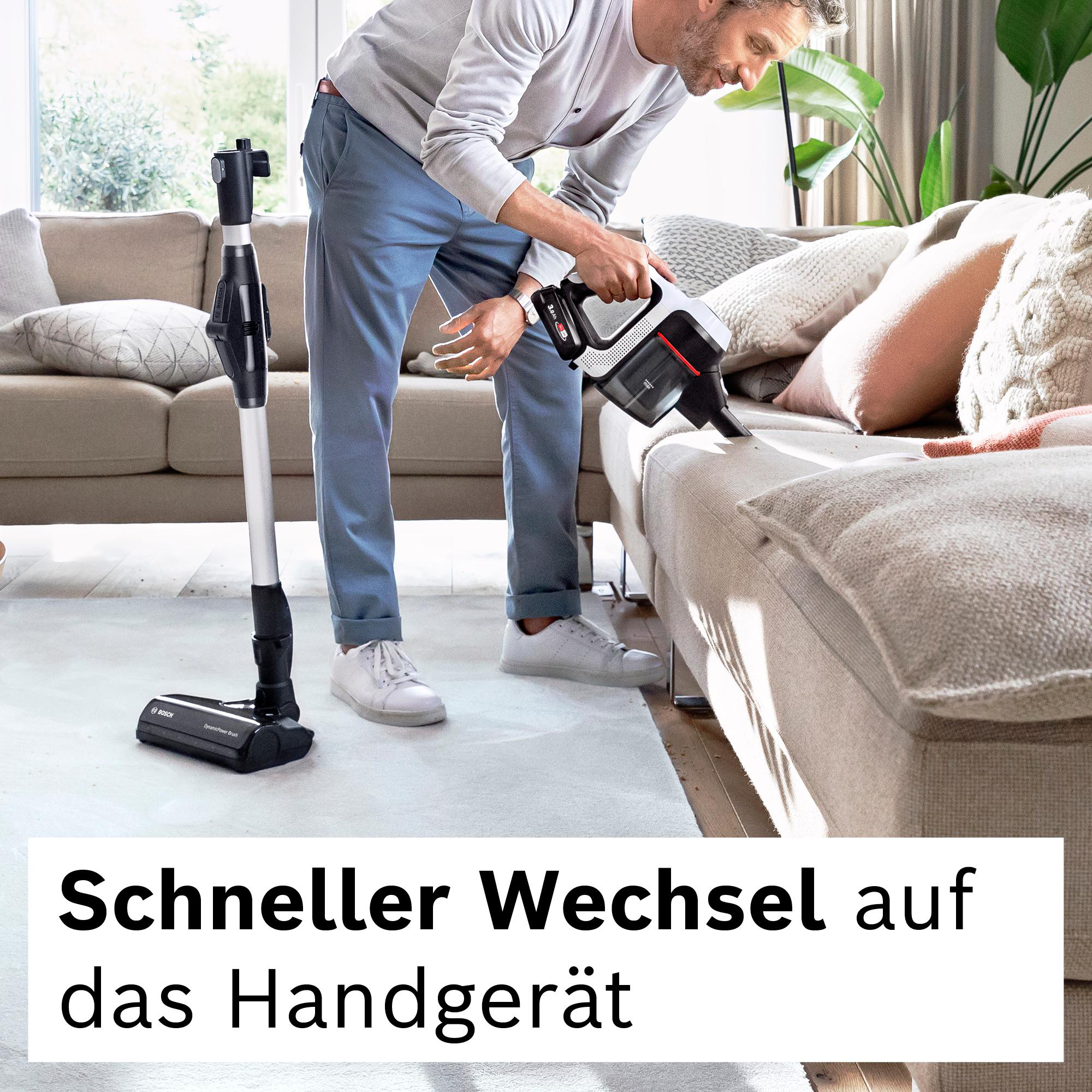 Ein Mann benutzt einen kabellosen Staubsauger auf einem Sofa. Der Staubsauger ist schwarz und weiß. Text: 'Schneller Wechsel auf das Handgerät'.