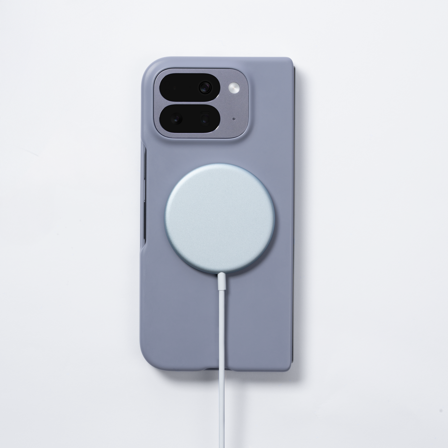Una funda de teléfono morada con un disco de carga azul claro, conectado por un cable blanco. El fondo es una superficie blanca lisa.
