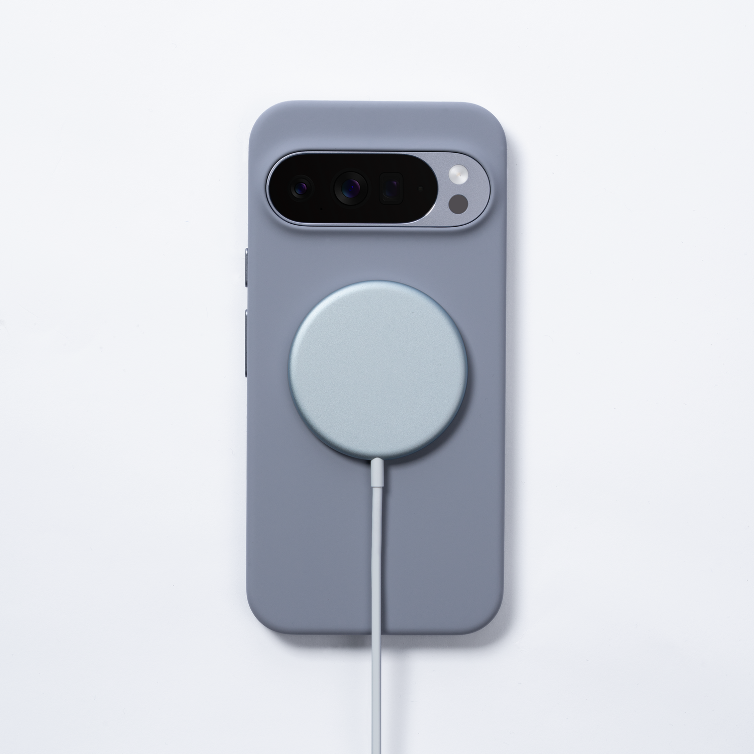Un teléfono gris en una funda con un cargador redondo adjunto. El teléfono tiene una cámara y el cargador un cable.