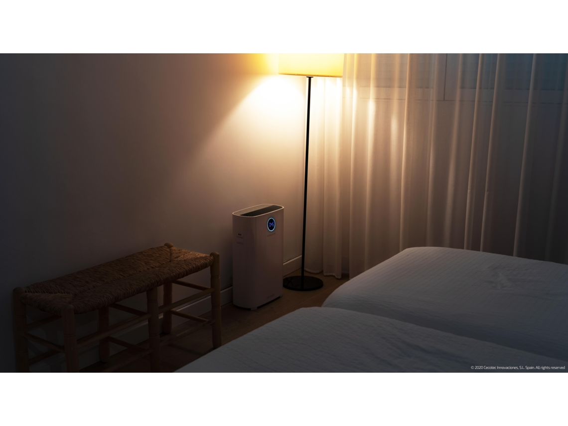 Un dormitorio con un purificador de aire blanco, banco, dos camas y una lámpara de pie. Cortinas transparentes a la derecha.