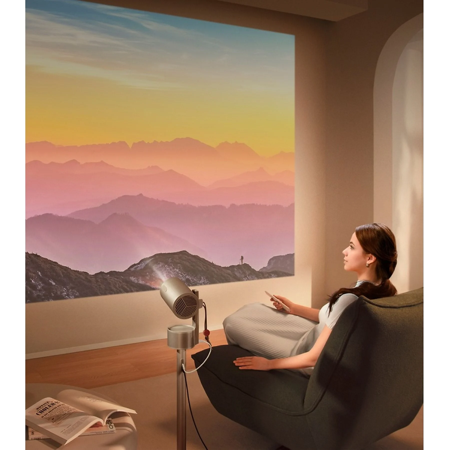 Een vrouw bekijkt een berglandschap dat op een muur wordt geprojecteerd. Een projector staat aan en een boek ligt open. Ze zit in een stoel.