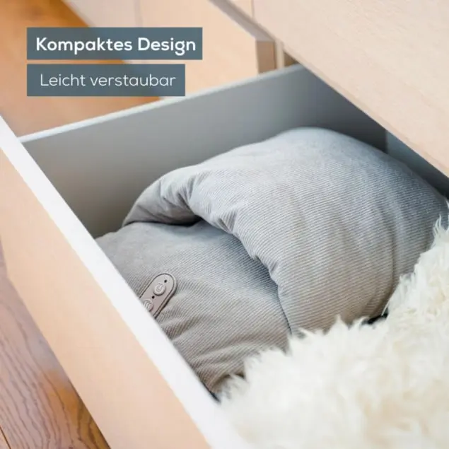 Ein graues Kissen mit Bedienfeld liegt in einer offenen Schublade. Rechts ist ein weißer, flauschiger Teppich zu sehen.