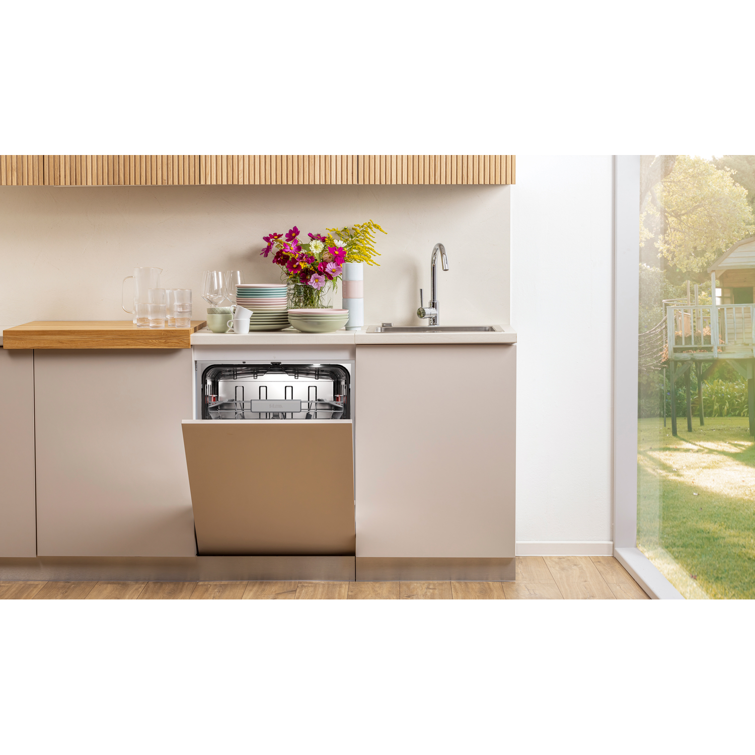 Een keuken met een open vaatwasser. Borden, bloemen en een gootsteen staan op het aanrecht. Een raam toont een boomhut in de achtertuin.