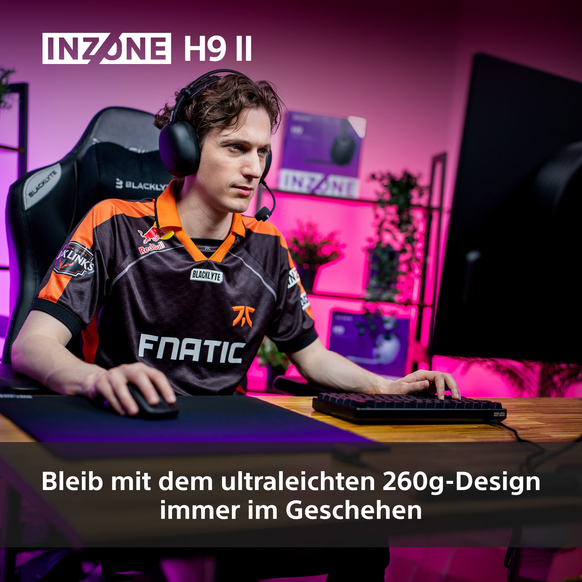 Ein Mann mit Headset, der Tastatur und Maus benutzt. Er trägt ein schwarz-orangenes Trikot. Es gibt einen Monitor und Pflanzen.