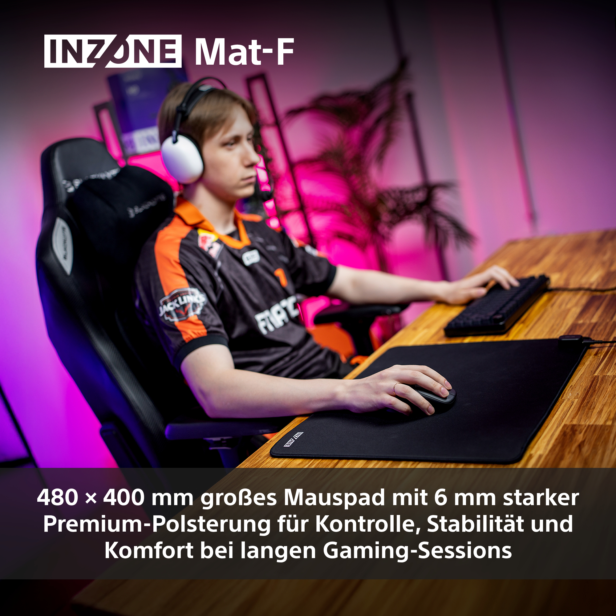 Ein Spieler mit Kopfhörern sitzt an einem Schreibtisch mit einem schwarzen Mauspadd und einer Tastatur. Der Schreibtisch ist holzmaseriert.