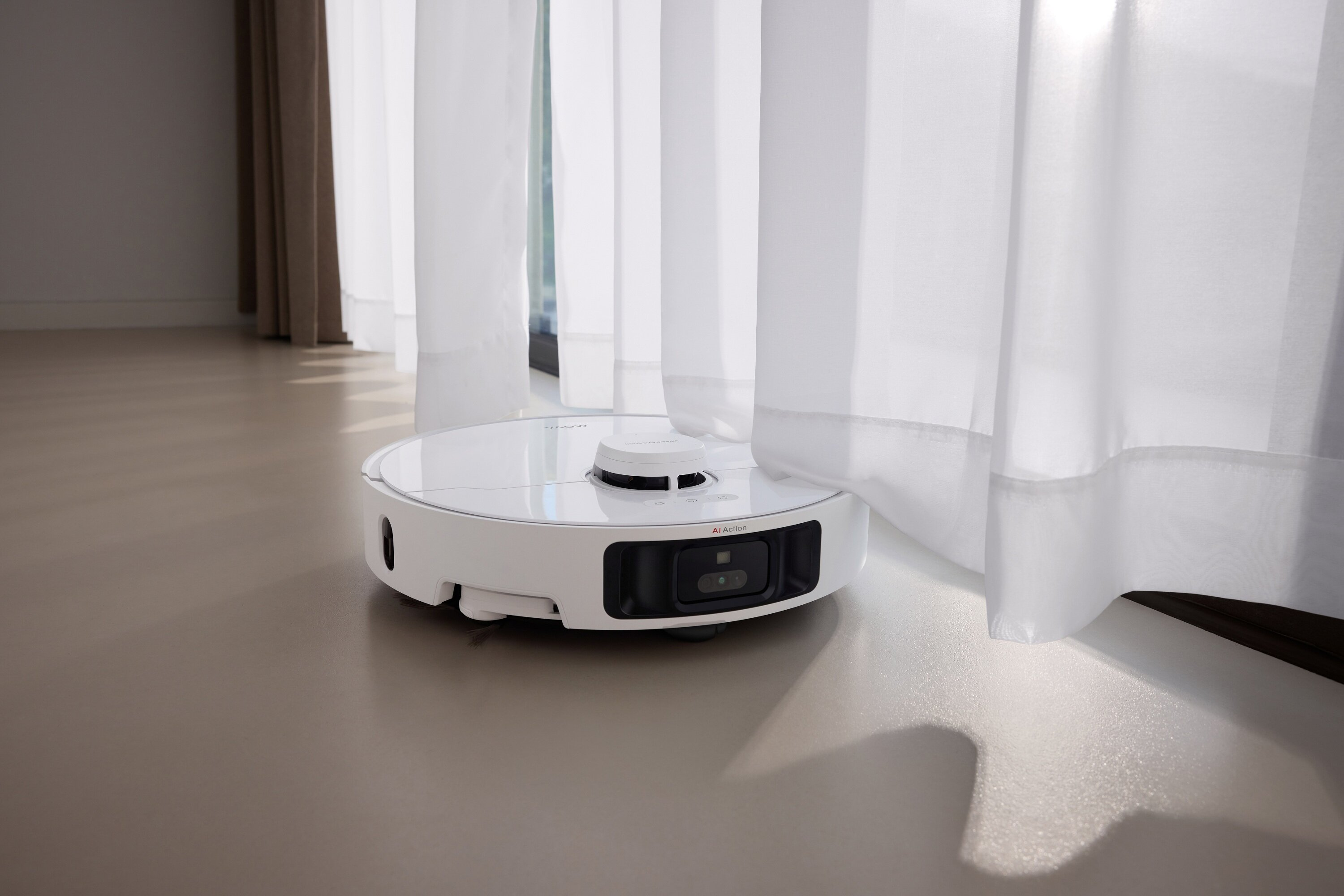 Biały odkurzacz robot stoi na jasnobrązowej podłodze. Białe zasłony w tle.