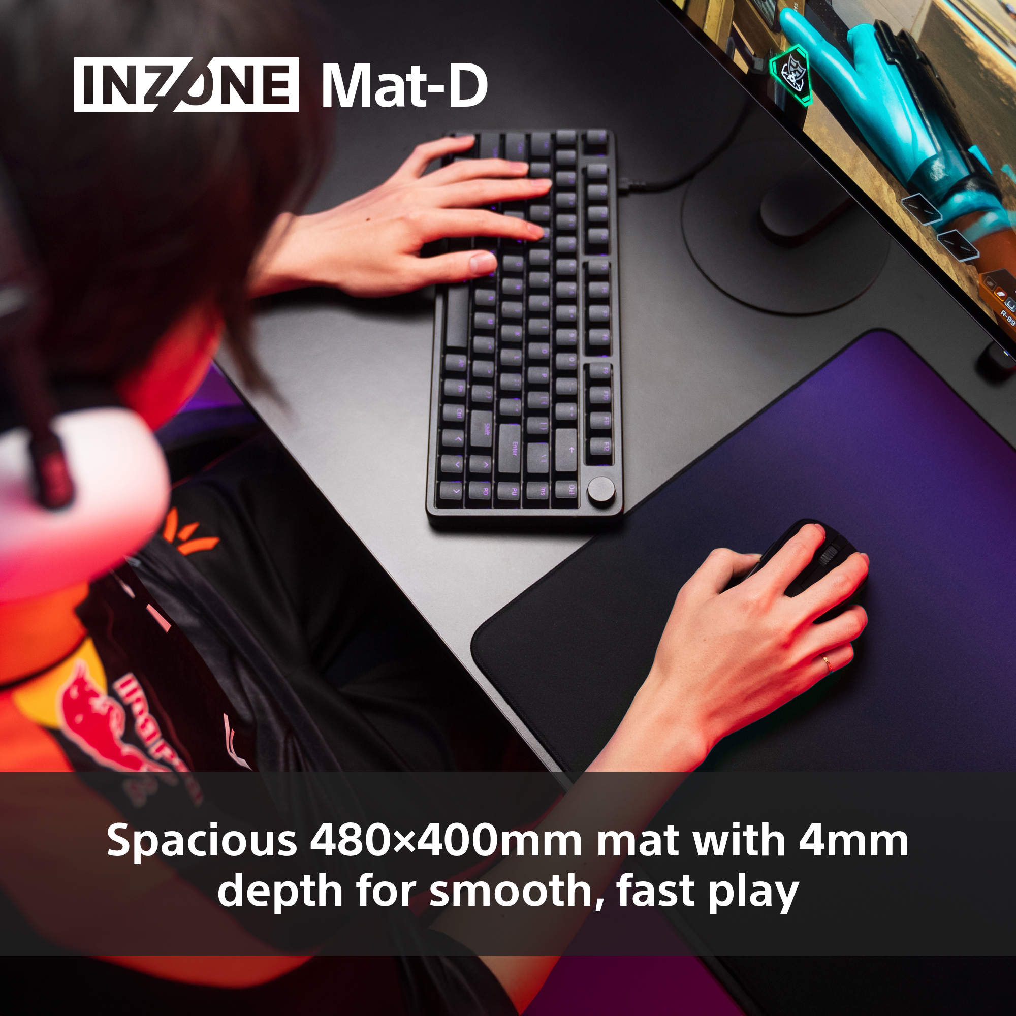Eine Person benutzt eine Tastatur und Maus auf einem Gaming-Setup. Die Matte ist schwarz und lila. Ein Monitor ist im Hintergrund.