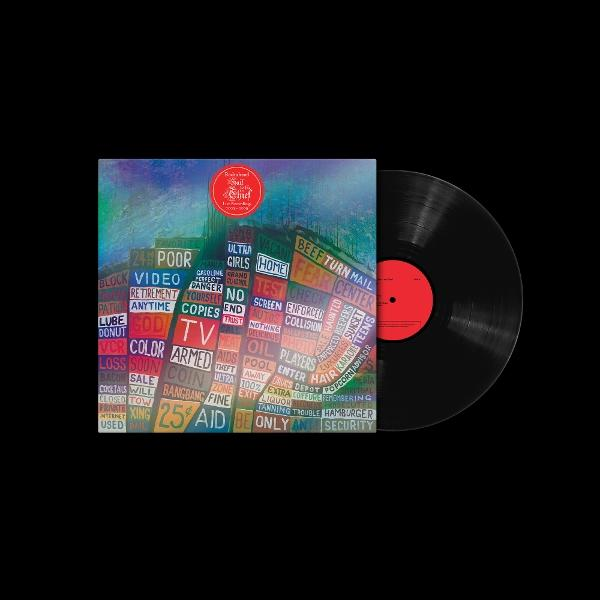 Eine Schallplatte mit einem bunten Albumcover, das verschiedene Wörter und einen roten Kreis zeigt. Die Schallplatte selbst ist schwarz mit rotem Mittellabel.